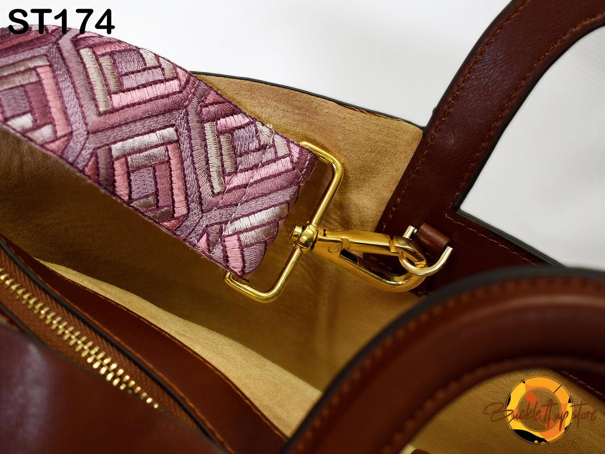 A close-up view of a brown leather handbag with a gold-colored metal strap attached to it.