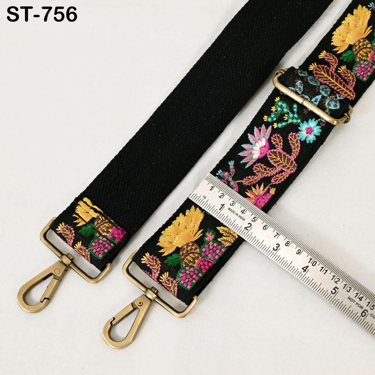 a black strap with colorful floral embroidery, and a ruler is placed next to it, indicating the strap's length.