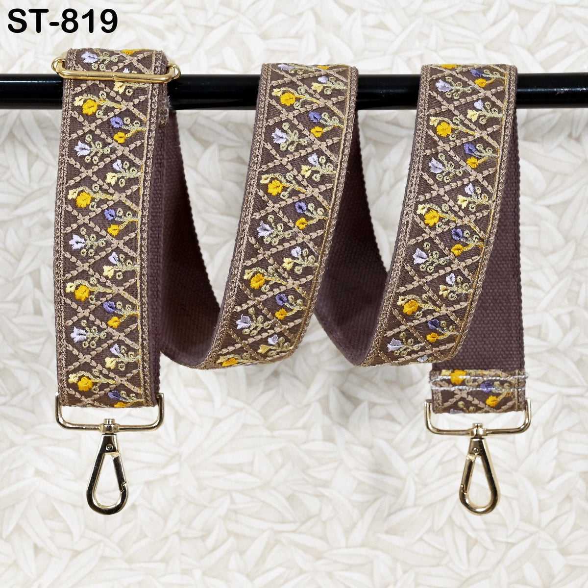 A brown strap with a floral pattern and gold hardware, hanging on a black rod.