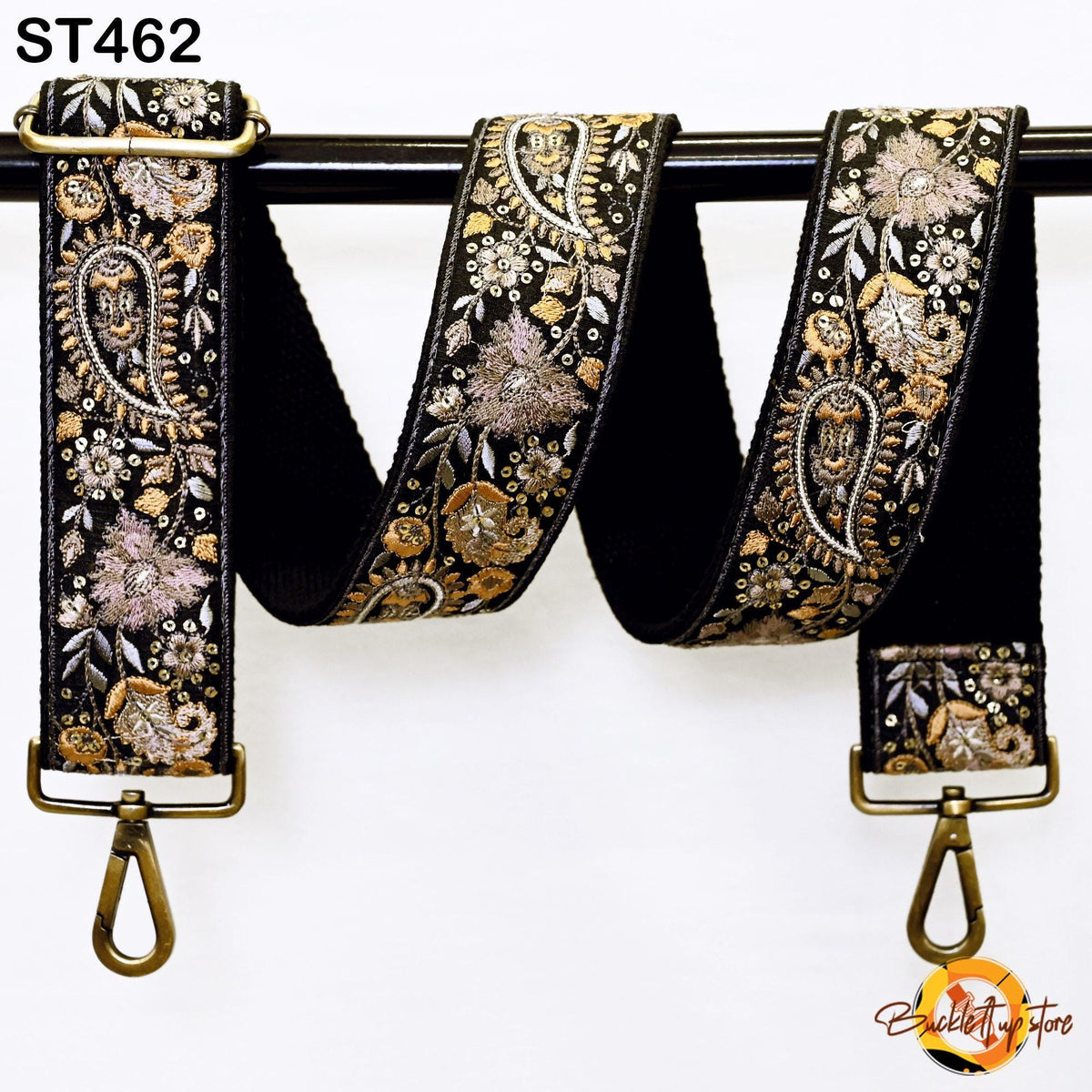 A black and gold embroidered strap with a floral pattern, hanging on a black rod.