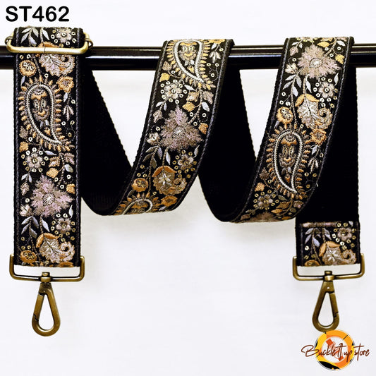 A black and gold embroidered strap with a floral pattern, hanging on a black rod.