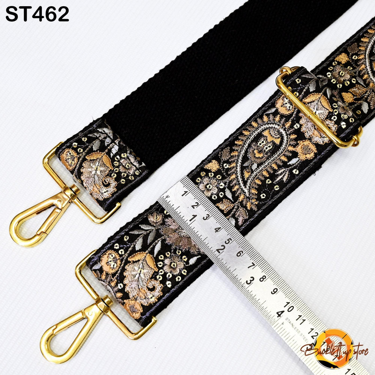 a black strap with a floral pattern and two gold-colored metal hooks, with a ruler placed between the straps to measure their length.