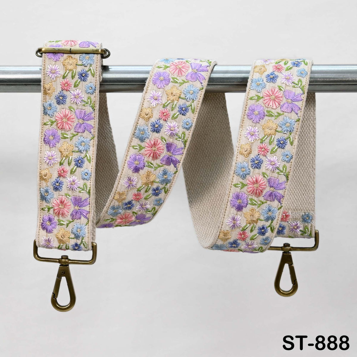 A floral-patterned beige strap with a metal clasp and hook attached to a metal bar.