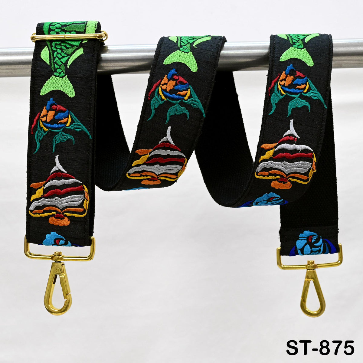 A colorful, embroidered strap with fish designs, hanging from a metal bar.