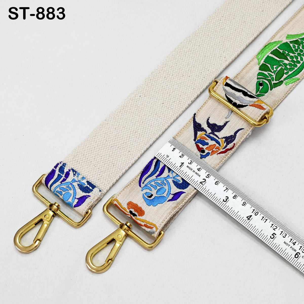 two colorful straps with fish designs, one white and one beige, placed on a white surface. There is a ruler placed next to the straps, indicating the size or length of the straps.