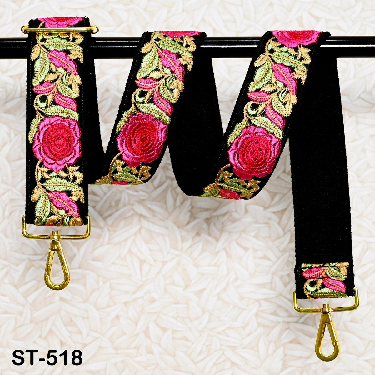 A black strap with a floral pattern in pink and green colors, hanging on a black rod.