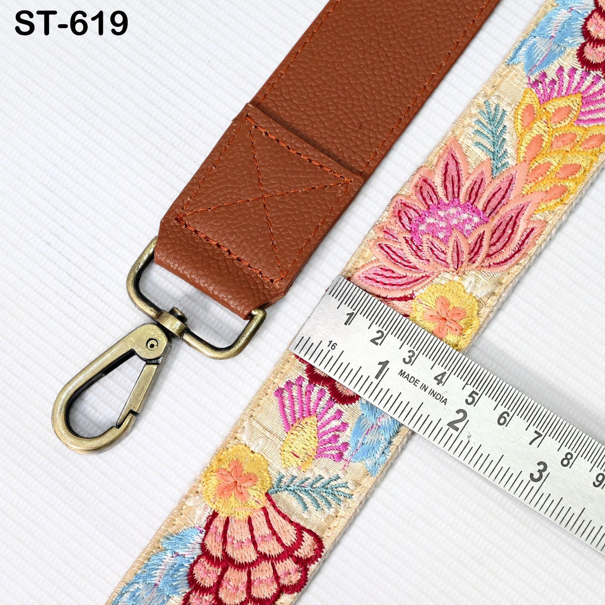 a brown leather strap with a floral pattern, a metal clasp, and a ruler for size comparison.