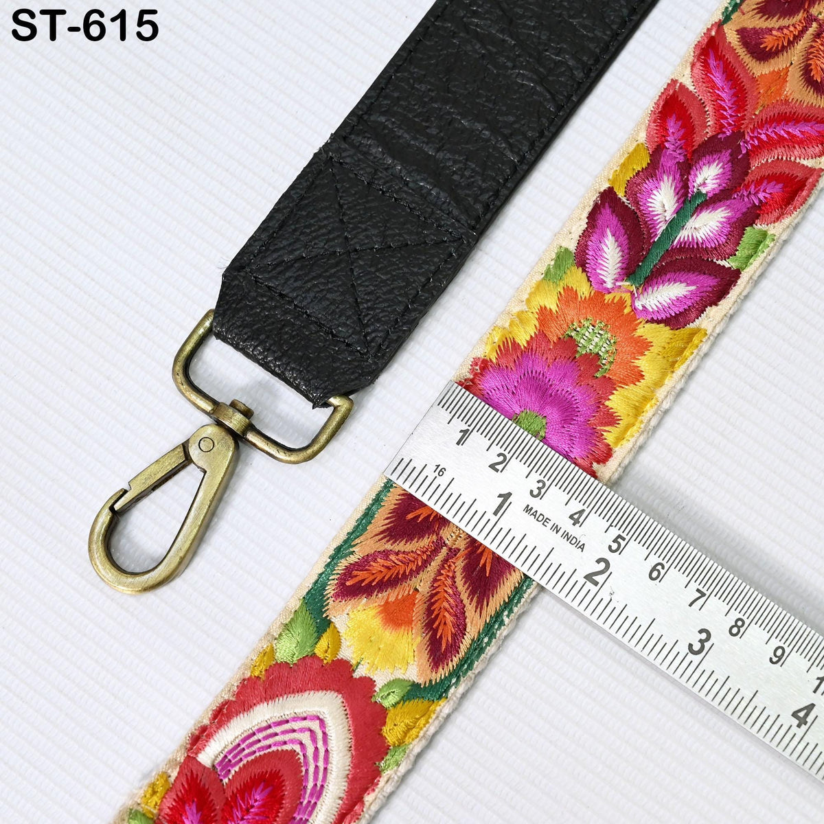 a black strap with a floral pattern and a gold-colored metal hook or clasp. A ruler is placed next to the strap, indicating the strap's length.