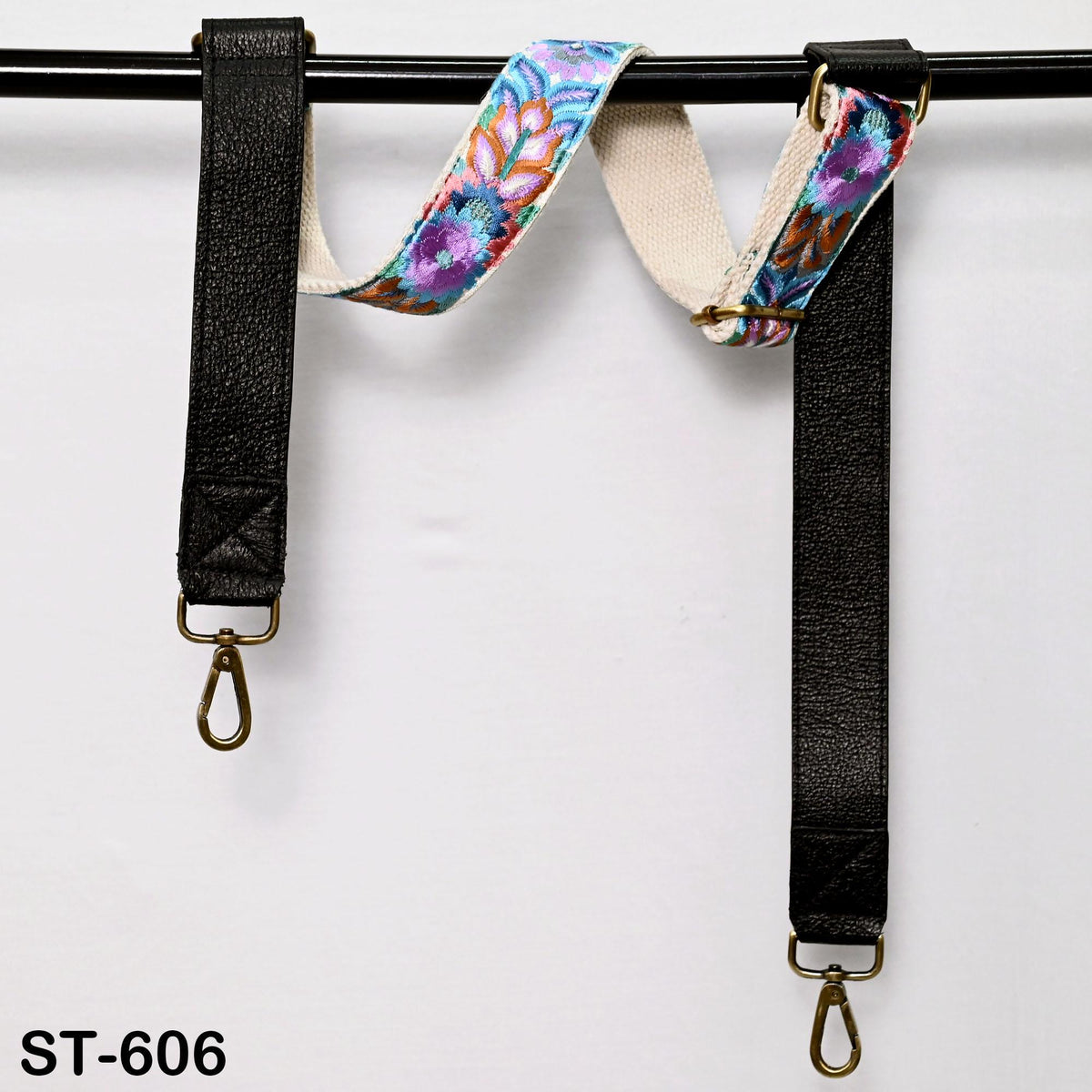 A pair of black leather straps with colorful floral patterns, hanging from a black metal bar.