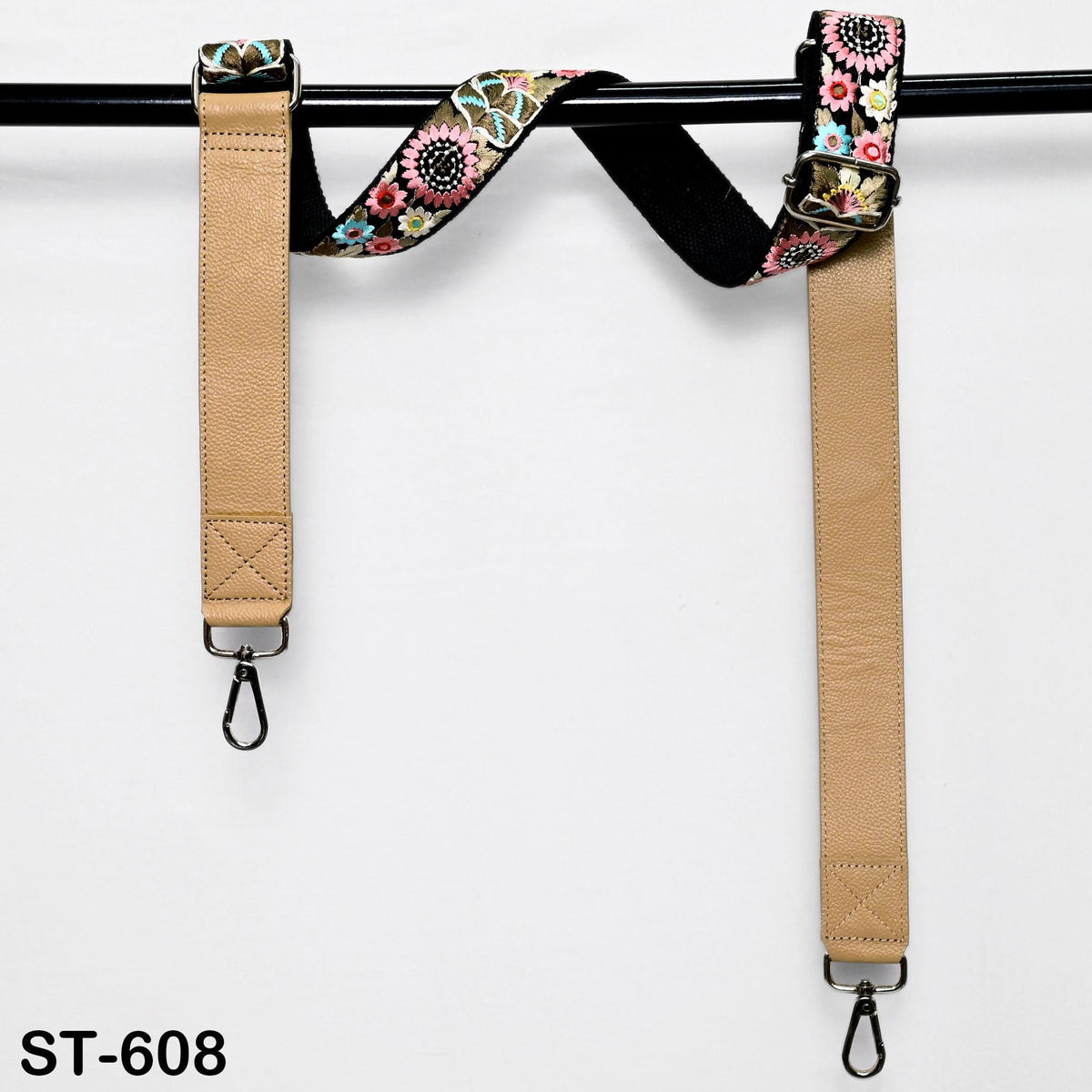 A pair of beige leather straps with floral patterns, hanging from a black bar.