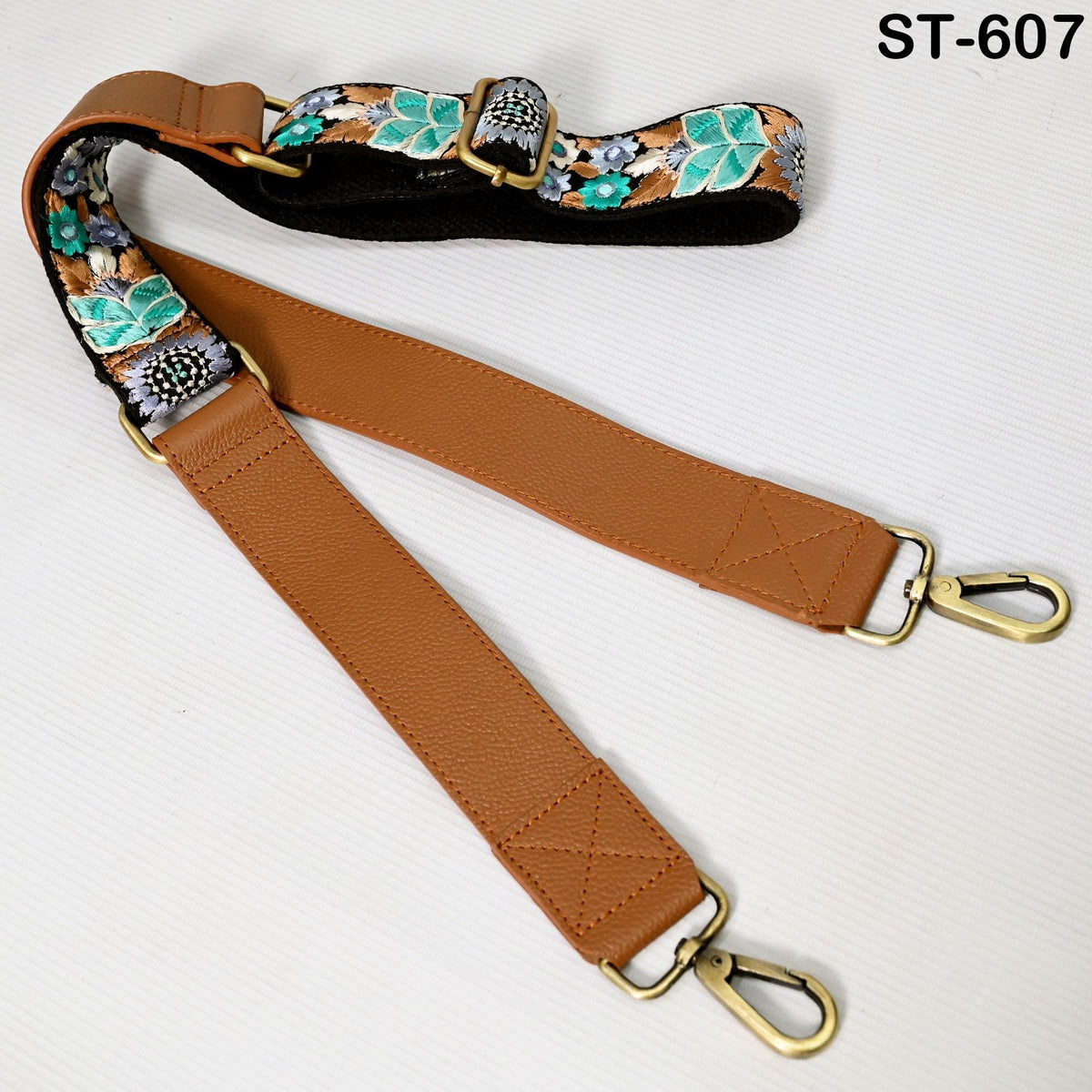 A brown leather strap with a floral pattern and two metal buckles, which appears to be a crossbody strap or strap for a bag.