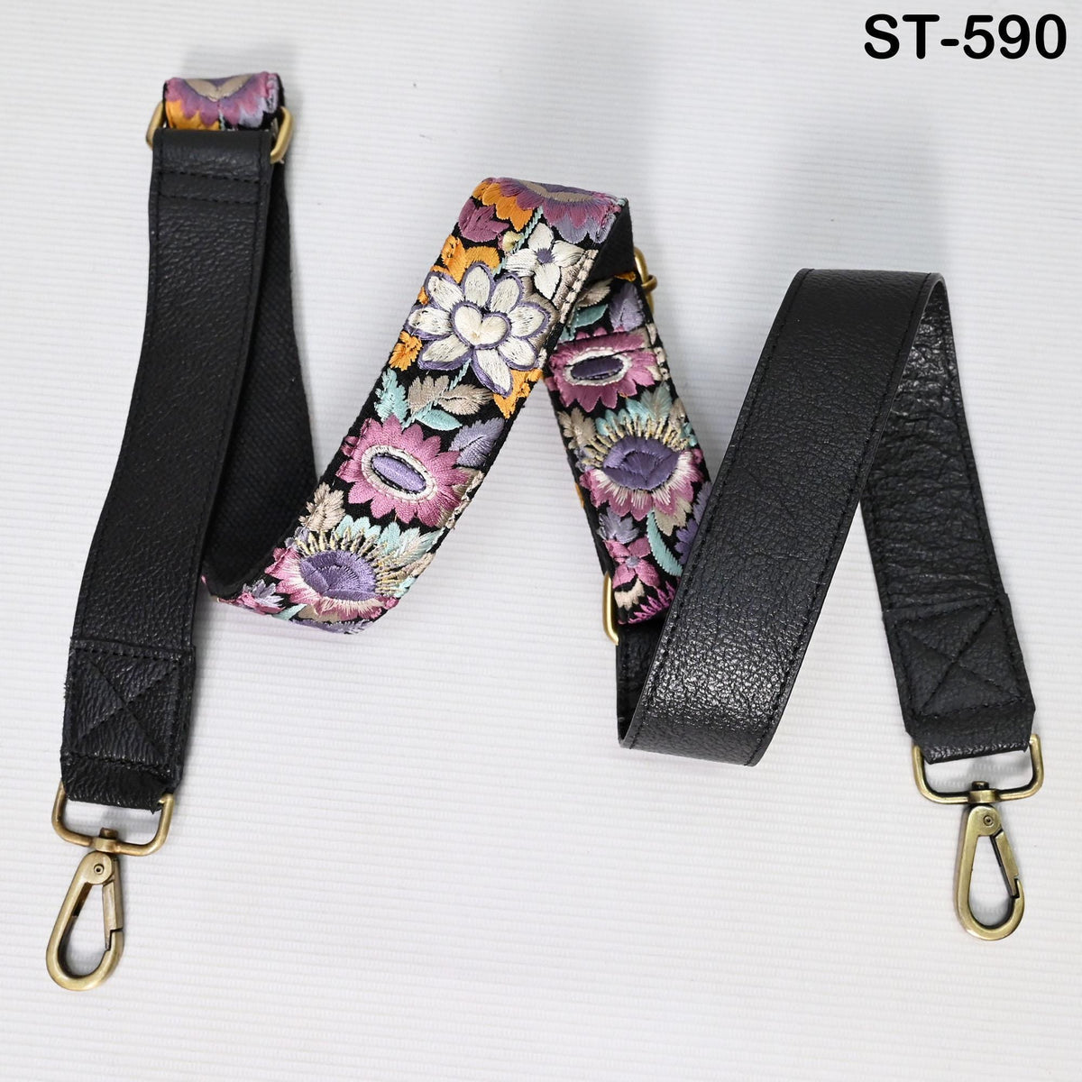 A floral patterned leather strap with a black leather strap attached to it, both with gold buckles.