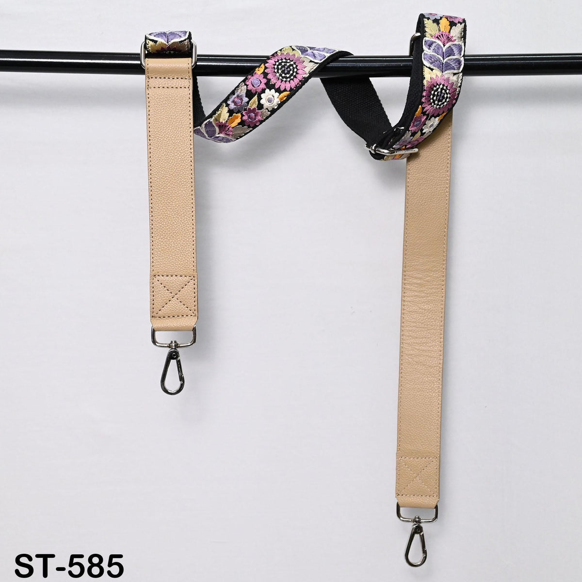 two beige straps with floral patterns hanging from a black bar.