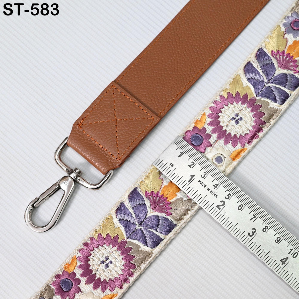 a brown leather strap with a floral pattern and a metal ruler placed next to it, indicating the strap's size.