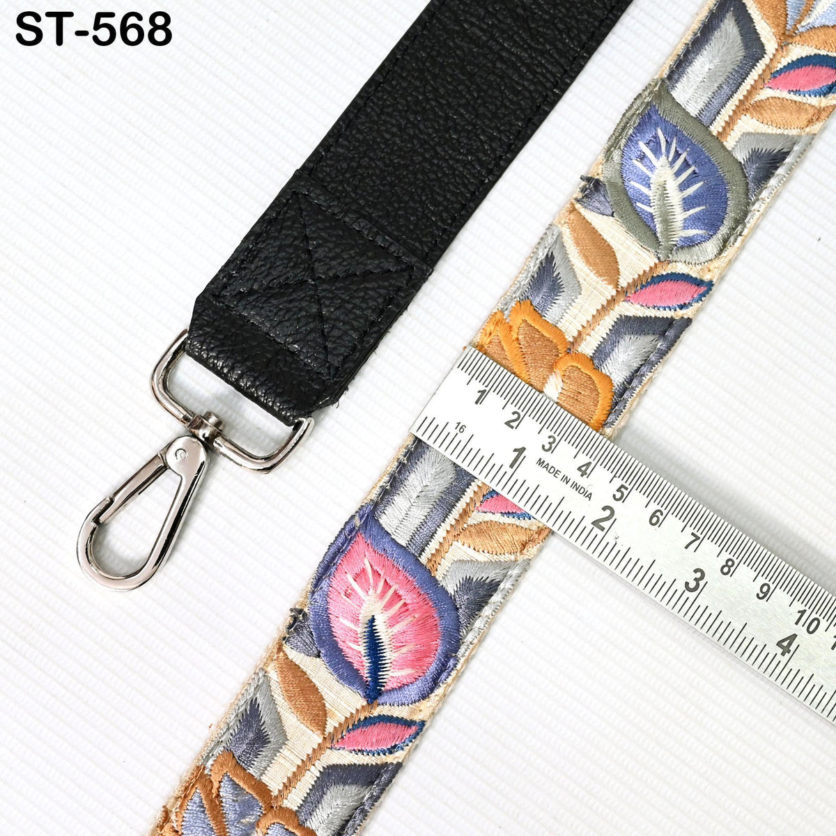 a black leather strap with a metal hook and a ruler placed on top of it, indicating the strap's length.