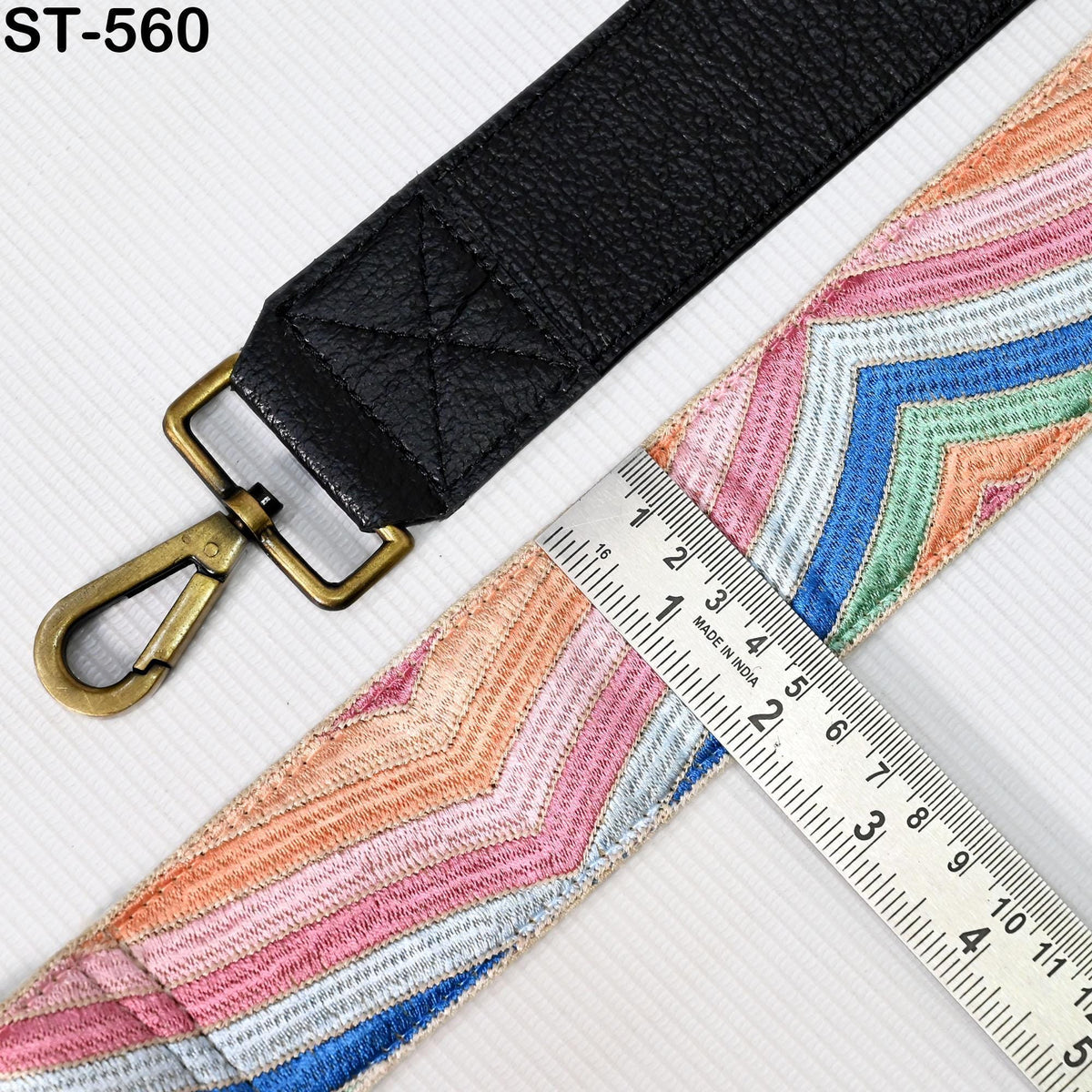 a black leather strap with a metal clasp and a colorful, patterned strap laid out on a white surface. There is a ruler placed next to the strap, indicating the size or length of the strap.