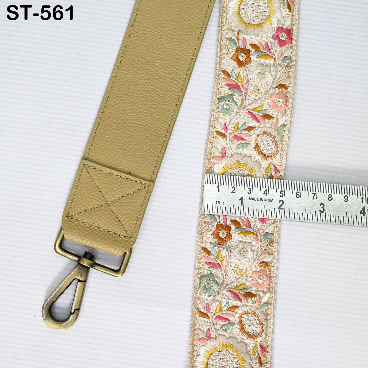 a beige leather strap with a floral pattern and a metal clasp, placed next to a ruler for size comparison.