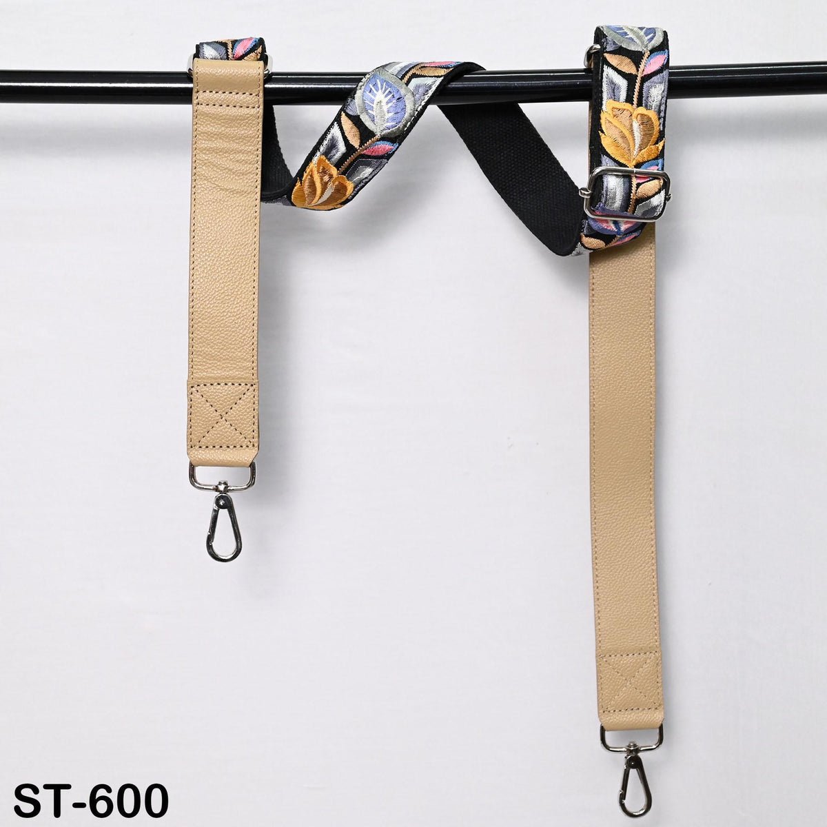 A pair of beige leather straps with colorful floral embroidery, hanging on a black bar.