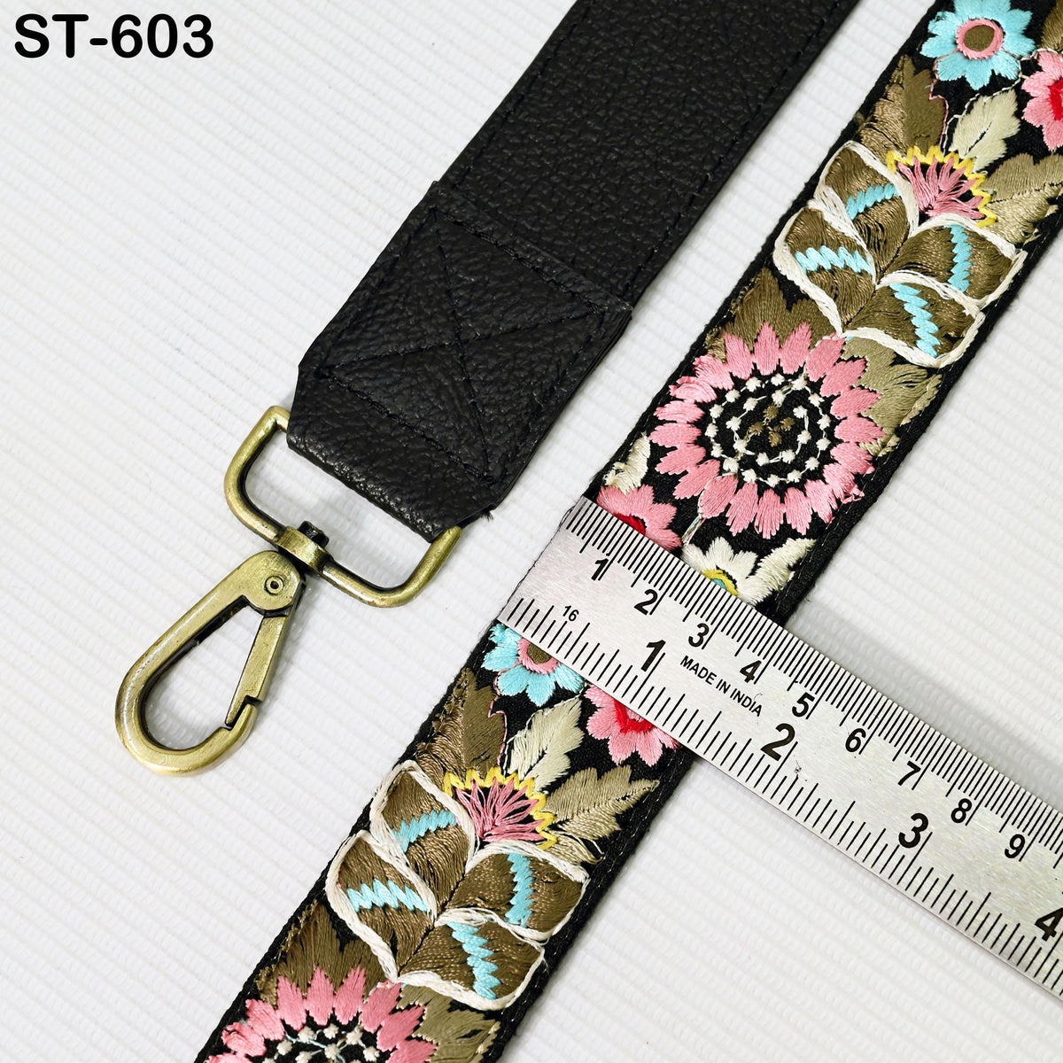a black strap with a floral pattern and a gold-colored metal clasp. A ruler is placed next to the strap, indicating the size or length of the strap.