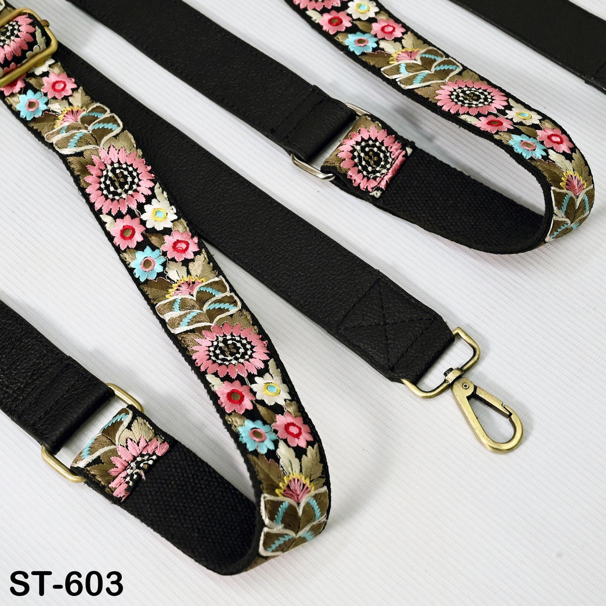a close-up view of a black strap with a floral pattern, featuring a gold-colored metal clasp.